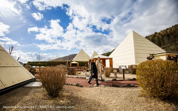 Teil des Galileo-Parks mit den pyramidenförmigen Gebäuden, in denen sich die Ausstellungen befinden. Zwei Freundinnen laufen durch den Park.