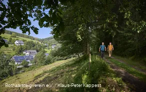 Zwei Wanderer im grünen Wald mit Ausblick auf den Ort Latrop am Rothaarsteig