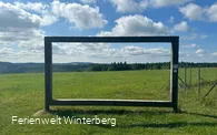 Landschaftsrahmen aus Holz mit Blick auf Wiesen und Wälder.