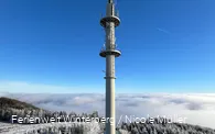 Fernmeldeturm umgeben von Schnee und Nebel vor blauem Himmel.