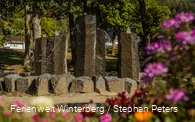 Ein steinerner Brunnen mit vier großen Steinsäulen, aus denen Wasser sprudelt.