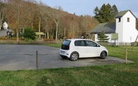 Parkplatz mit einem weißen geparkten Auto und einer kleinen Kapelle im Hintergrund.