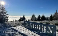 Tisch mit Metallschild mit der Aufschrift Hesborn umgeben von Wald, blauem Himmel und strahlender Sonne im Winter.