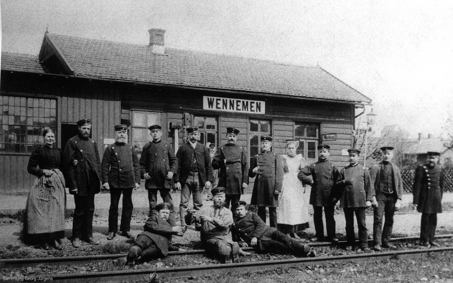 Das erste Bahnhofsgebäude von Wennemen um 1873. Der Zugverkehr scheint noch selten zu sein, sonst hätte man sich nicht zum Umtrunk und Foto im Gleis versammeln können