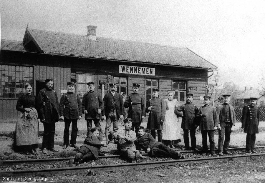 Das erste Bahnhofsgebäude von Wennemen um 1873. Der Zugverkehr scheint noch selten zu sein, sonst hätte man sich nicht zum Umtrunk und Foto im Gleis versammeln können
