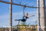 Eine Frau hängt an einem Sitzgurt an einer Metallschiene und breitet die Arme aus.