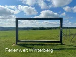 Landschaftsrahmen aus Holz mit Blick auf Wiesen und Wälder.
