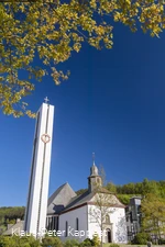 Eine Kirche neben einem hohen Kirchturm mit Turmuhr vor blauem Himmel.
