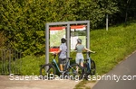 Ein Radfahrerpärchen steht mit ihren Rädern vor einer Info-Tafel des SauerlandRadrings und liest.