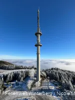 Fernmeldeturm umgeben von Schnee und Nebel vor blauem Himmel.
