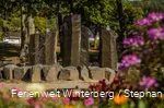 Ein steinerner Brunnen mit vier großen Steinsäulen, aus denen Wasser sprudelt.