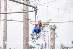 Eine Frau hängt in einem Sitzgurt an einer Metallschiene und breitet die Arme aus.
