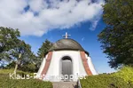 Eine Kapelle umgeben von Bäumen vor blauem Himmel.