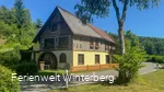 Ein altes Gebäude mit Fachwerk und einem Wasserrad an der seitlichen Hauswand.